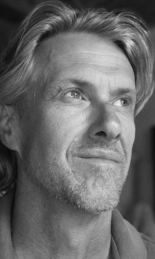 A close-up black and white portrait of a client with light hair and stubble, he's preferred product is Rishi extract